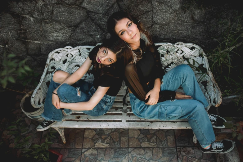 two women sitting on a bench in front of a stone wall