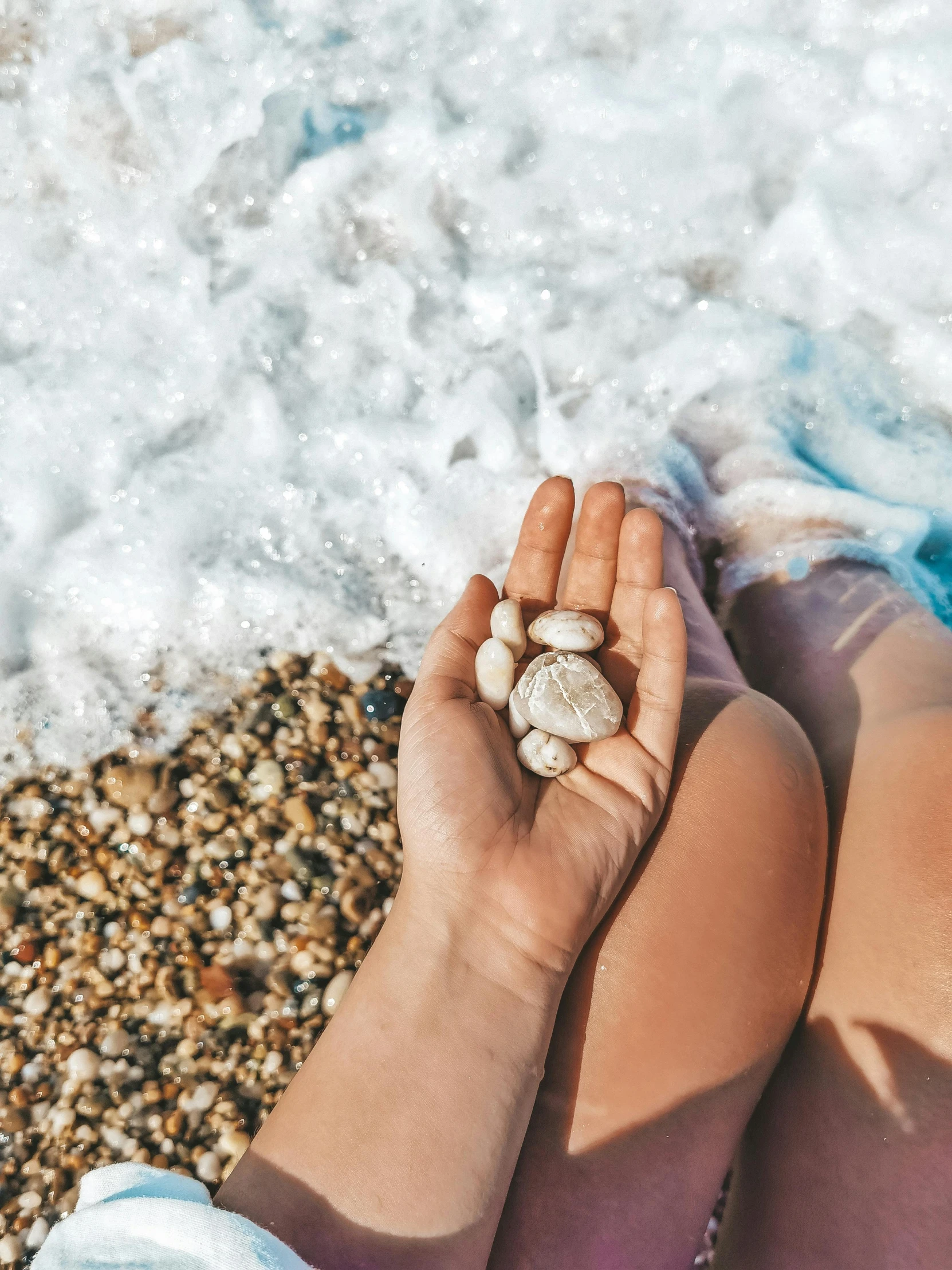 a woman in a blue shirt holding her foot on the beach with shells