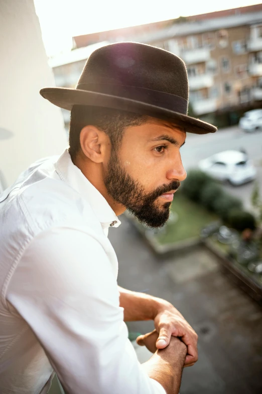 a bearded man wearing a black fedora standing next to a building