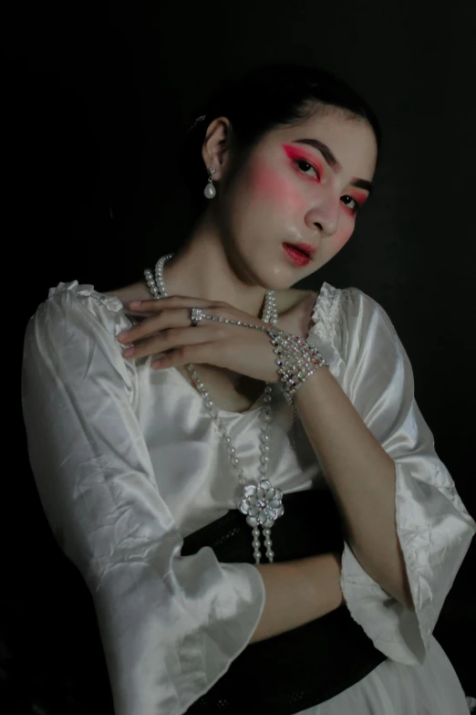 a woman in white with makeup wearing pearls