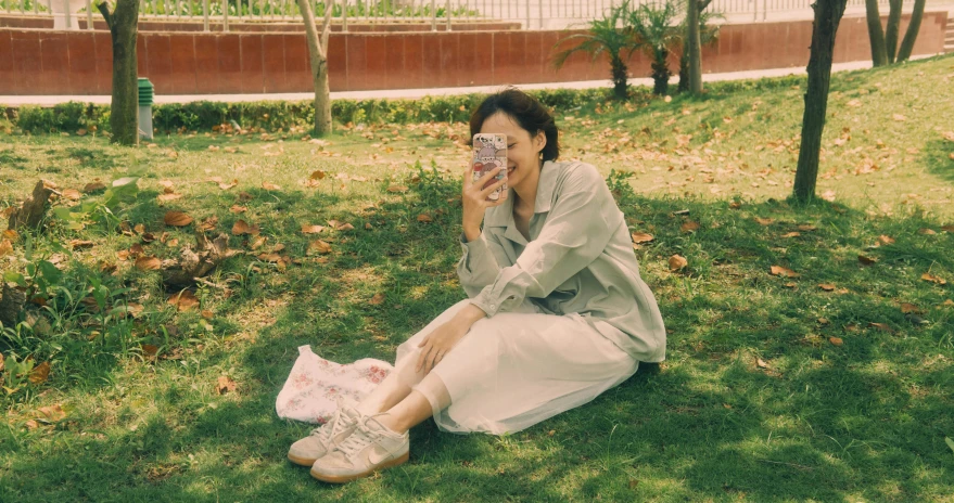 woman in dress taking pograph of herself sitting on grass