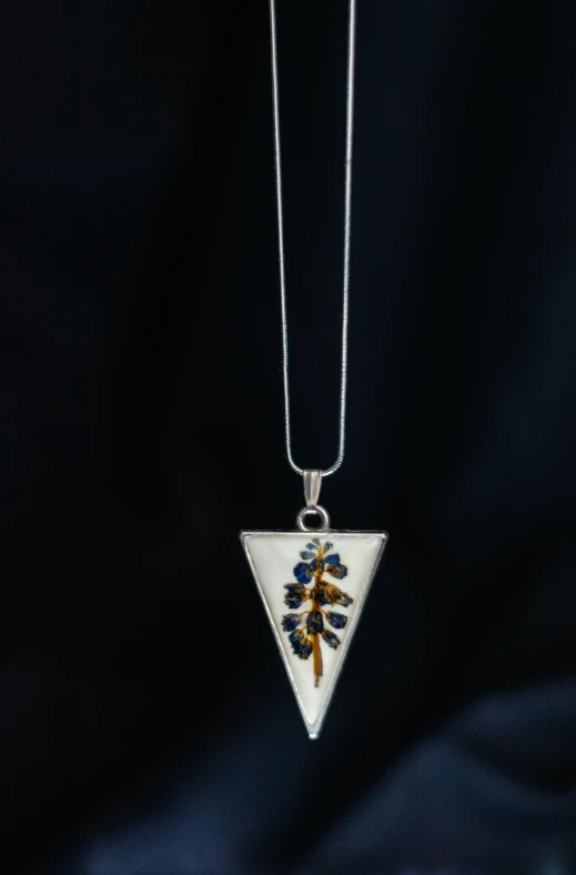 a white triangle pendant with colorful flowers is on a necklace