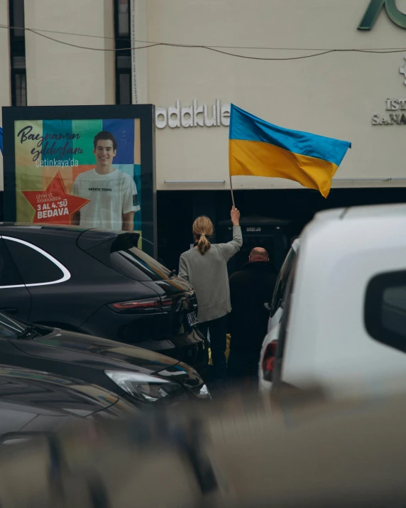 a woman holding up a flag and two banners in a parking lot