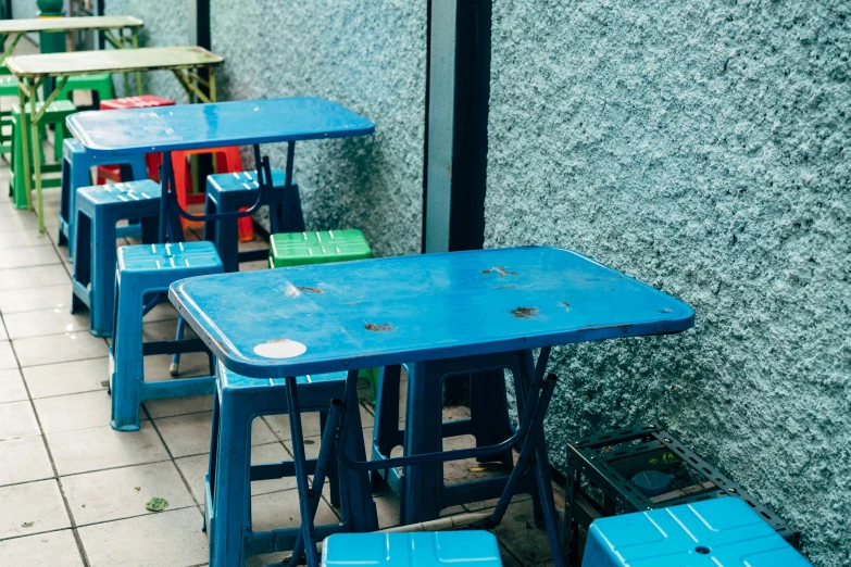 blue tables and chairs sit outside in front of a cement wall