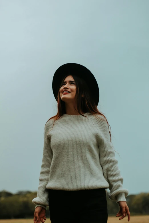 a woman in black hat and white sweater with her arms wide open