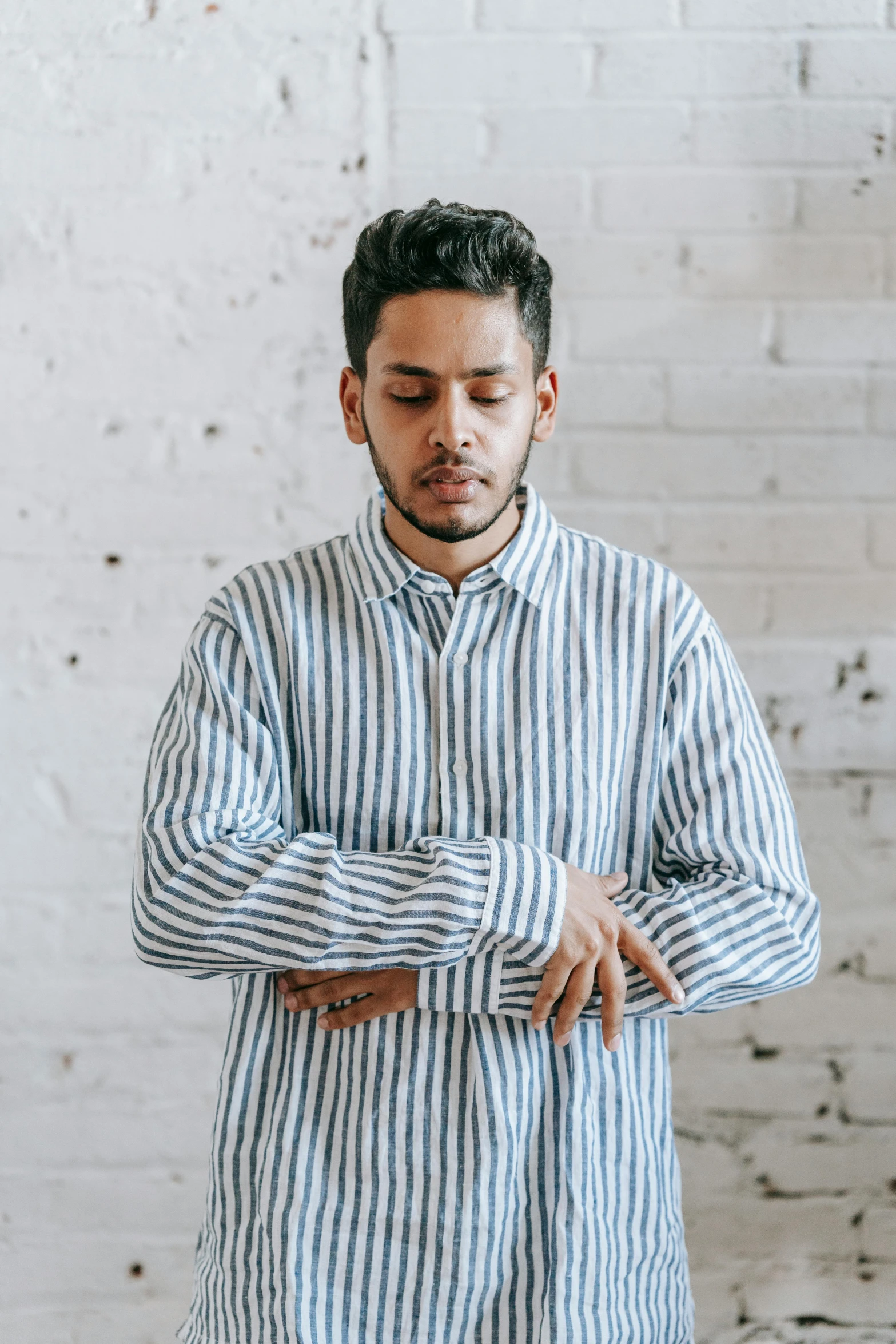 a man in a striped shirt stands looking down and his hands are folded