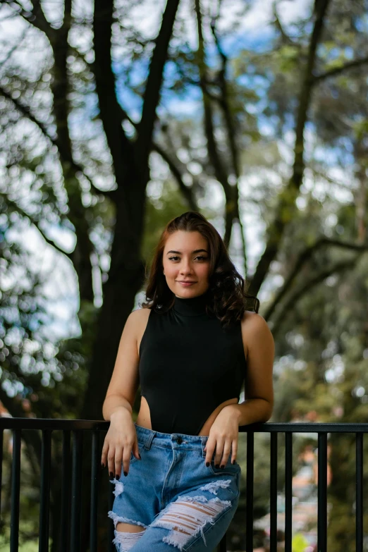 a young woman leans against a fence, wearing torn blue denim shorts