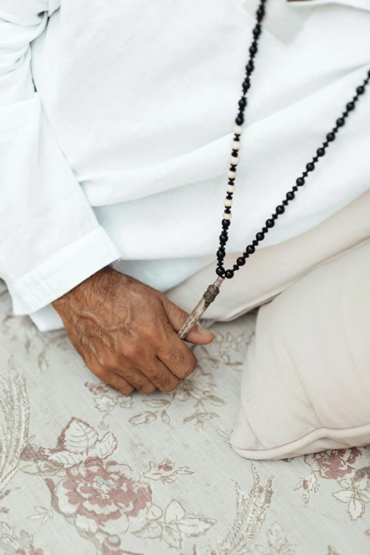 a man holds a black beaded necklace and wears it with a white shirt