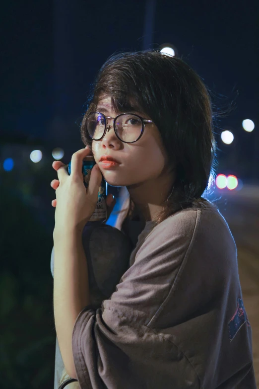 a woman in glasses is on her cell phone at night