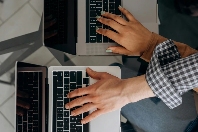 two hands on laptops, one of them is typing