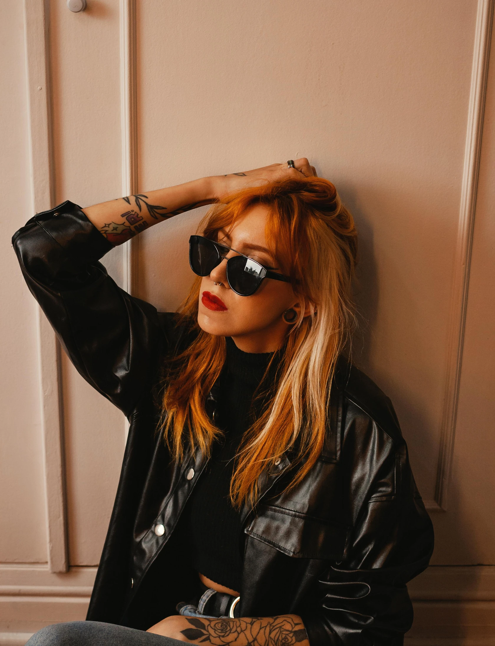 a young woman with a black jacket and sunglasses, leaning against a wall