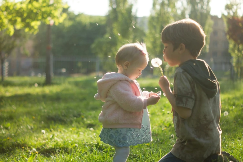 two young children blow on a dandelion