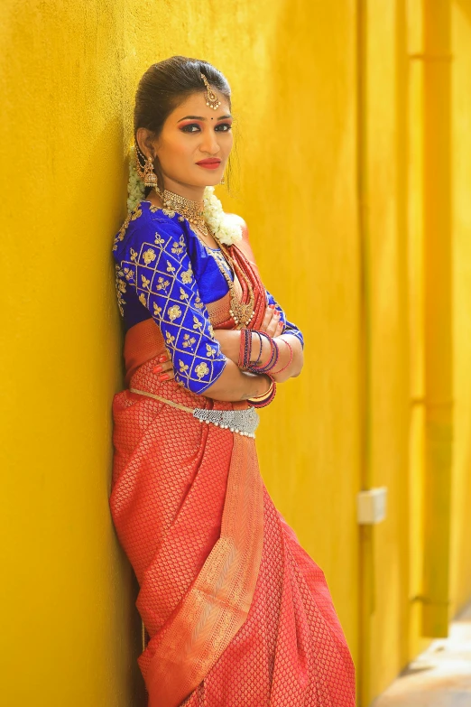 a woman standing against a yellow wall wearing a red and blue sari