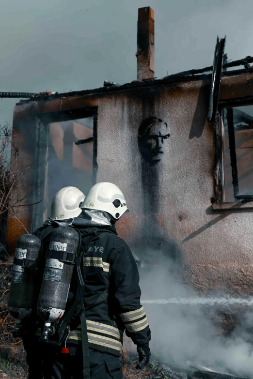 two firemen standing outside of an burned out house