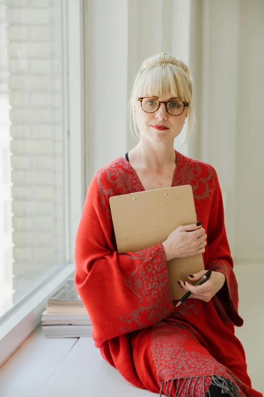 a woman sitting in front of a window holding a file