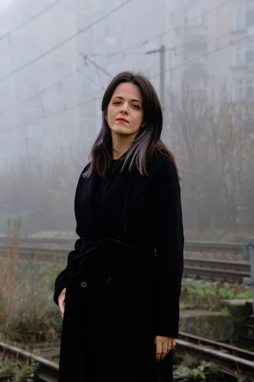 woman standing with her arms behind her back on a train track in fog