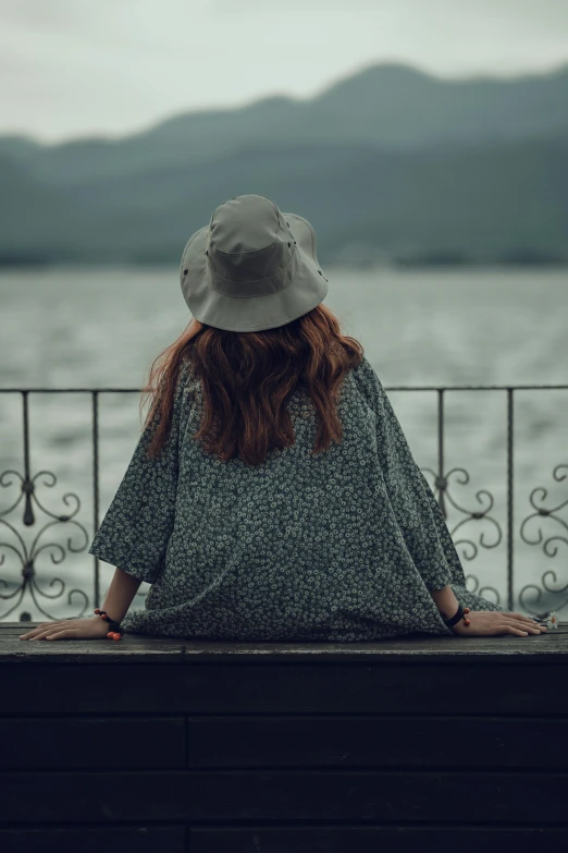 a woman is sitting on a fence looking out over the water