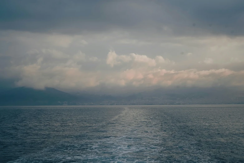 an ocean view with the clouds and some hills in the distance