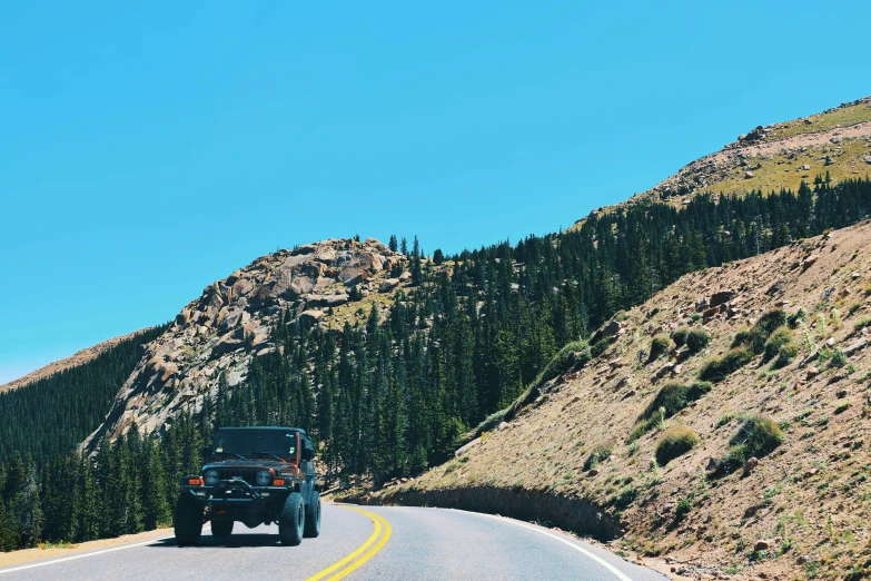 a jeep driving down a mountainous road near a mountain