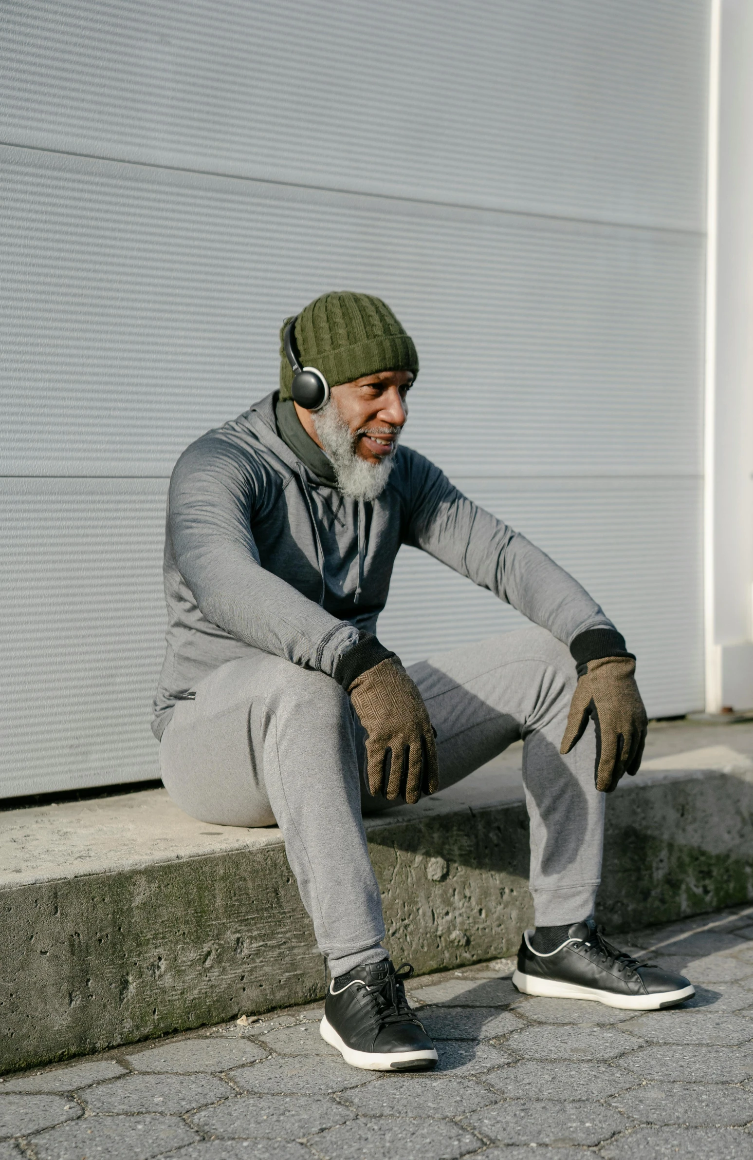 an old man with a hat and knit cap sitting on concrete step outside of a garage door