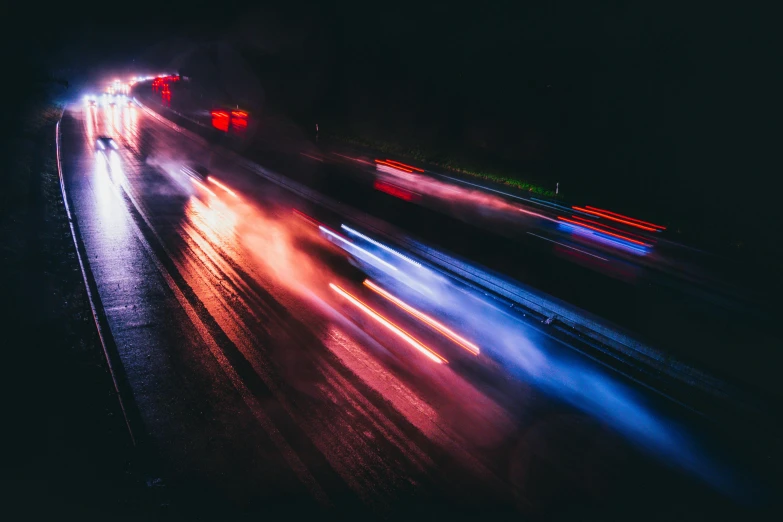 cars are speeding past on a city street at night