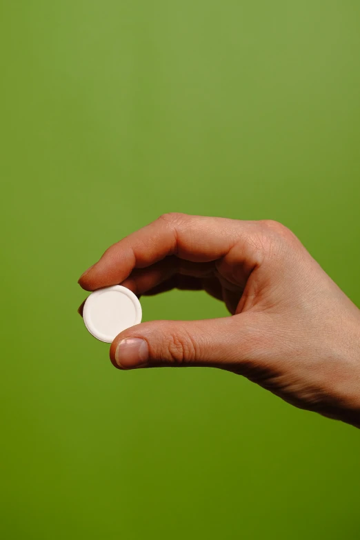 the hand holds the white condom on a green background