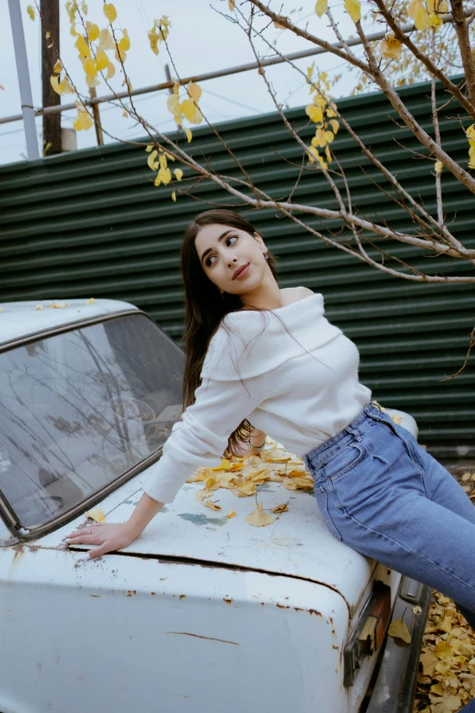woman leaning on an old car parked in front of leafy tree