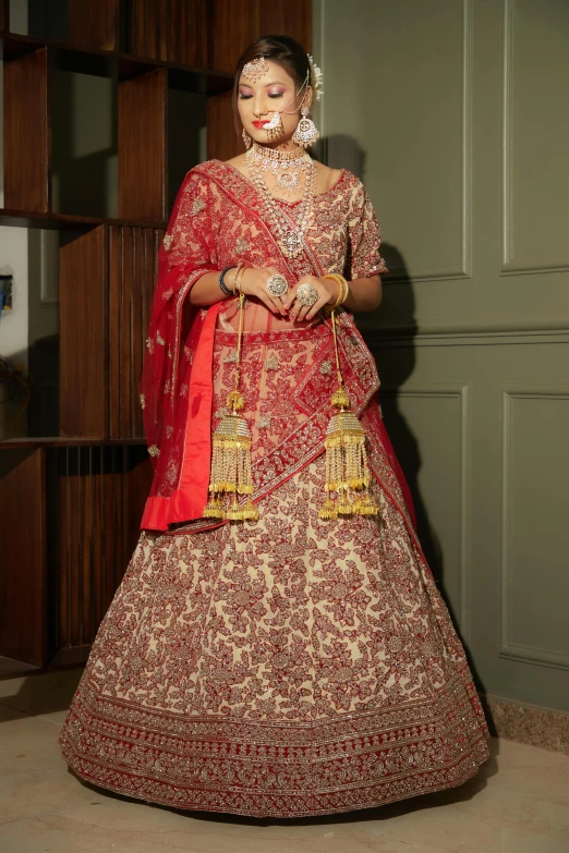 a woman in a red and gold lehenga stands in a green room