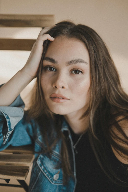 young woman with long hair in denim jacket sitting on bench