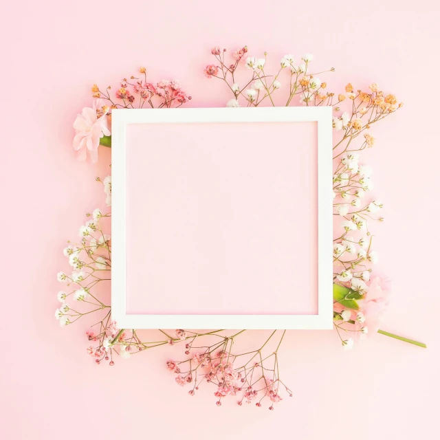 a white frame surrounded by flowers against a pink background