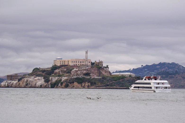 large boat sailing near rocky shoreline with city on hill in background