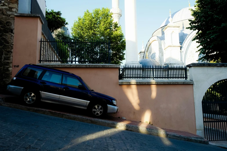 a blue car parked beside an iron fence next to a tower