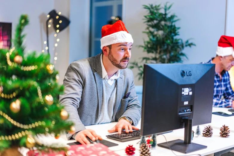 an office worker wears a santa's hat at his desk