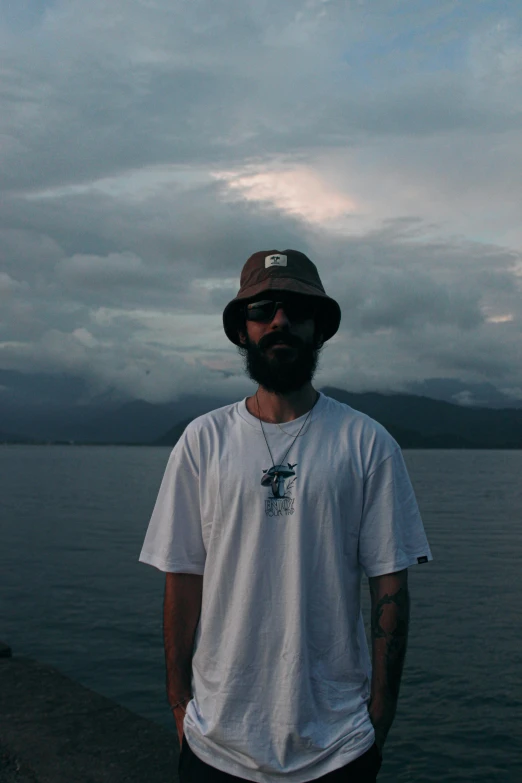 a man with a hat and sunglasses stands by the water