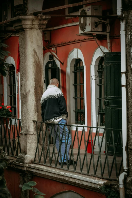 man leaning on a balcony with red wall and black railing