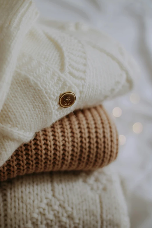 a close up of three folded sweaters on a bed