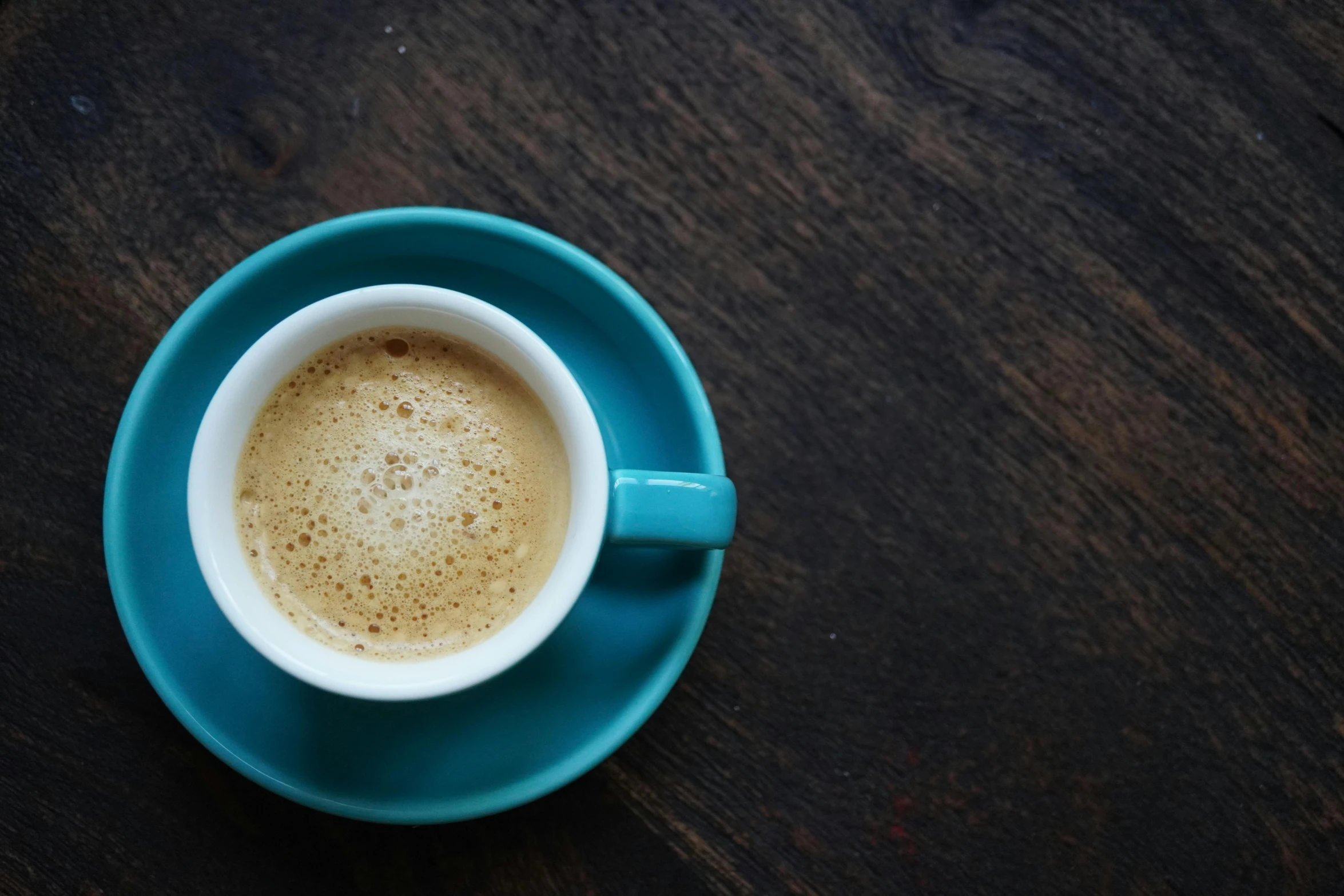 cup filled with light brown coffee on a dark wooden table