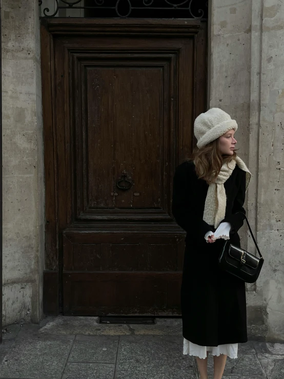 a woman in a black coat and white hat standing on the street