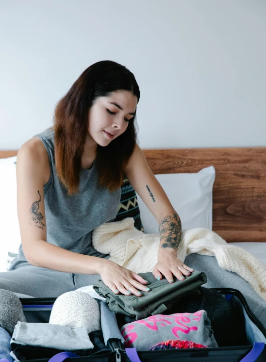 a woman holds an open suitcase with clothing on the bed