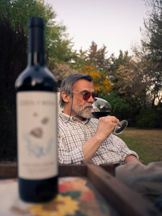 man sitting in a chair looking at a glass with wine next to him