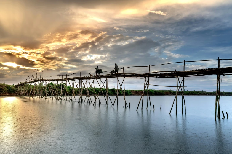 the sun sets behind a bridge that is over water