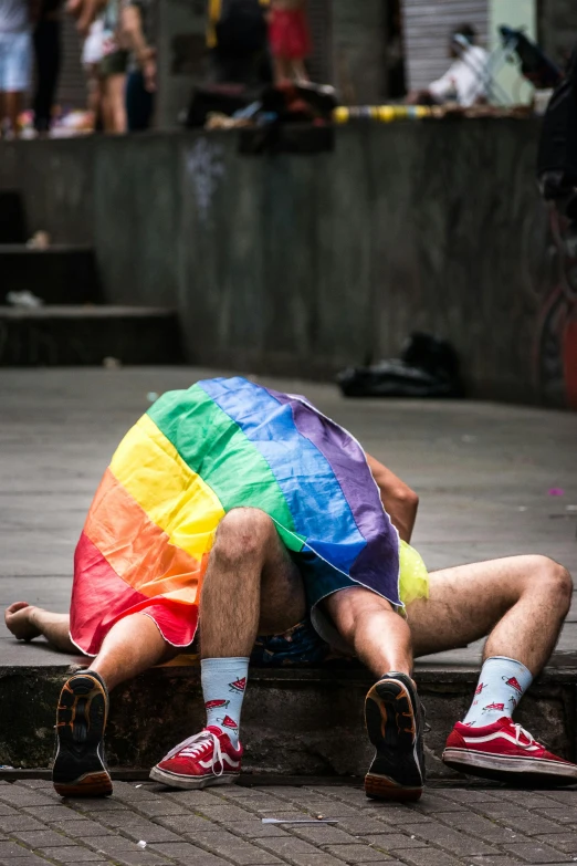 a man is sitting on the curb with a rainbow colored rainbow umbrella