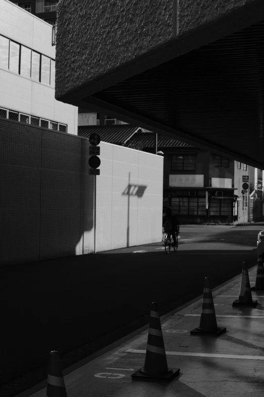 black and white pograph of a construction area with traffic lights, cones, and pedestrian on sidewalk