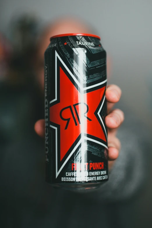 person holding up an energy drink with black and red colors