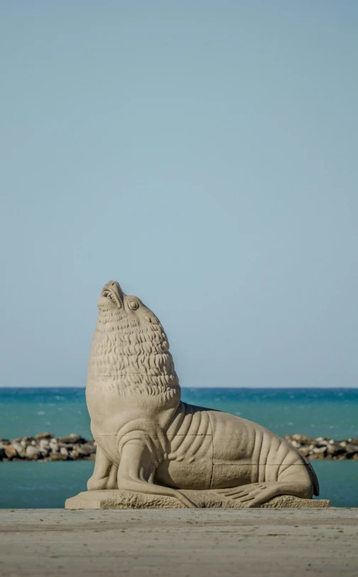 a statue sitting on the sand in front of an ocean