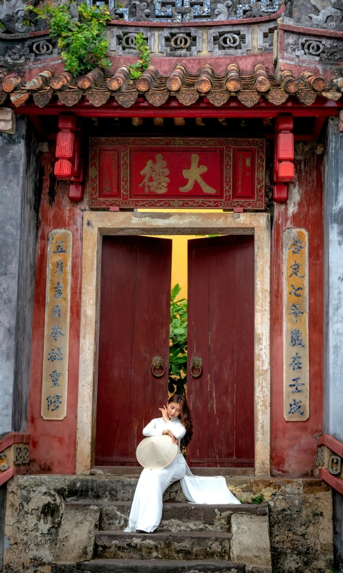 a woman dressed up with traditional chinese clothing poses at the door to an old building