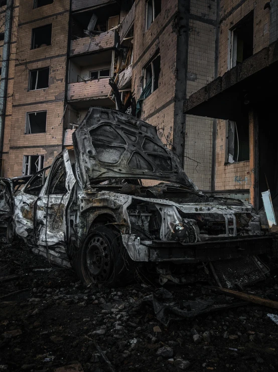 a dirty car with a broken hood in front of a tall building