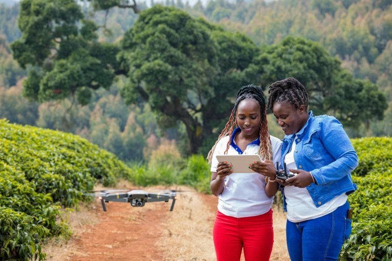 two women stand in a tea field using an ipad