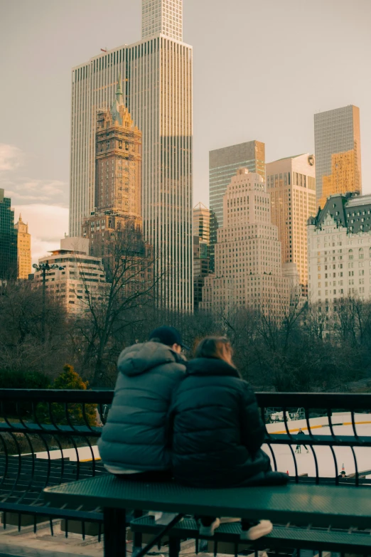 two people sit next to each other on a bench with city skyline in the background