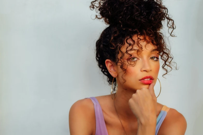 a woman with curly hair and earrings is holding her hand on her lip